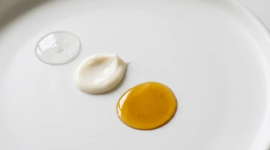 Composizione minimalista di prodotti skincare stratificati con texture diverse su superficie pulita